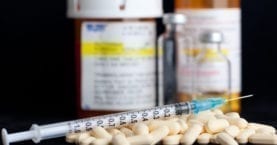 Syringe, pills with drug vials in background