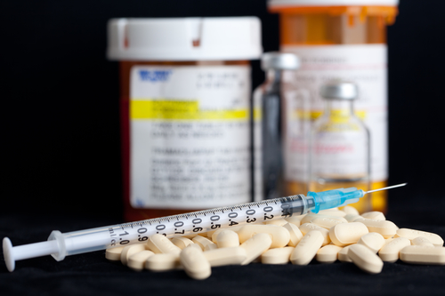 Syringe, pills with drug vials in background